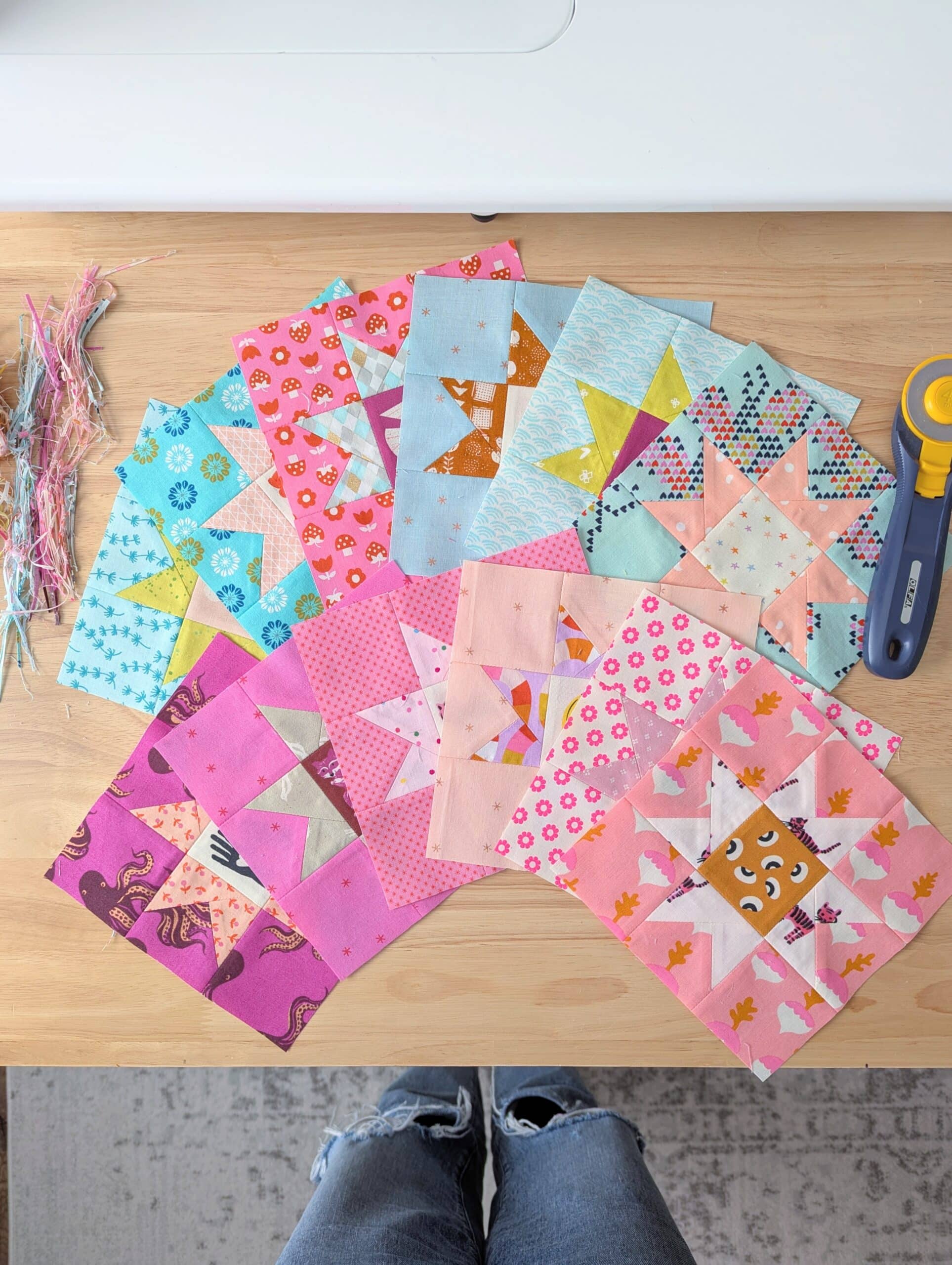 Colourful quilt blocks are fanned out on a wooden table.
