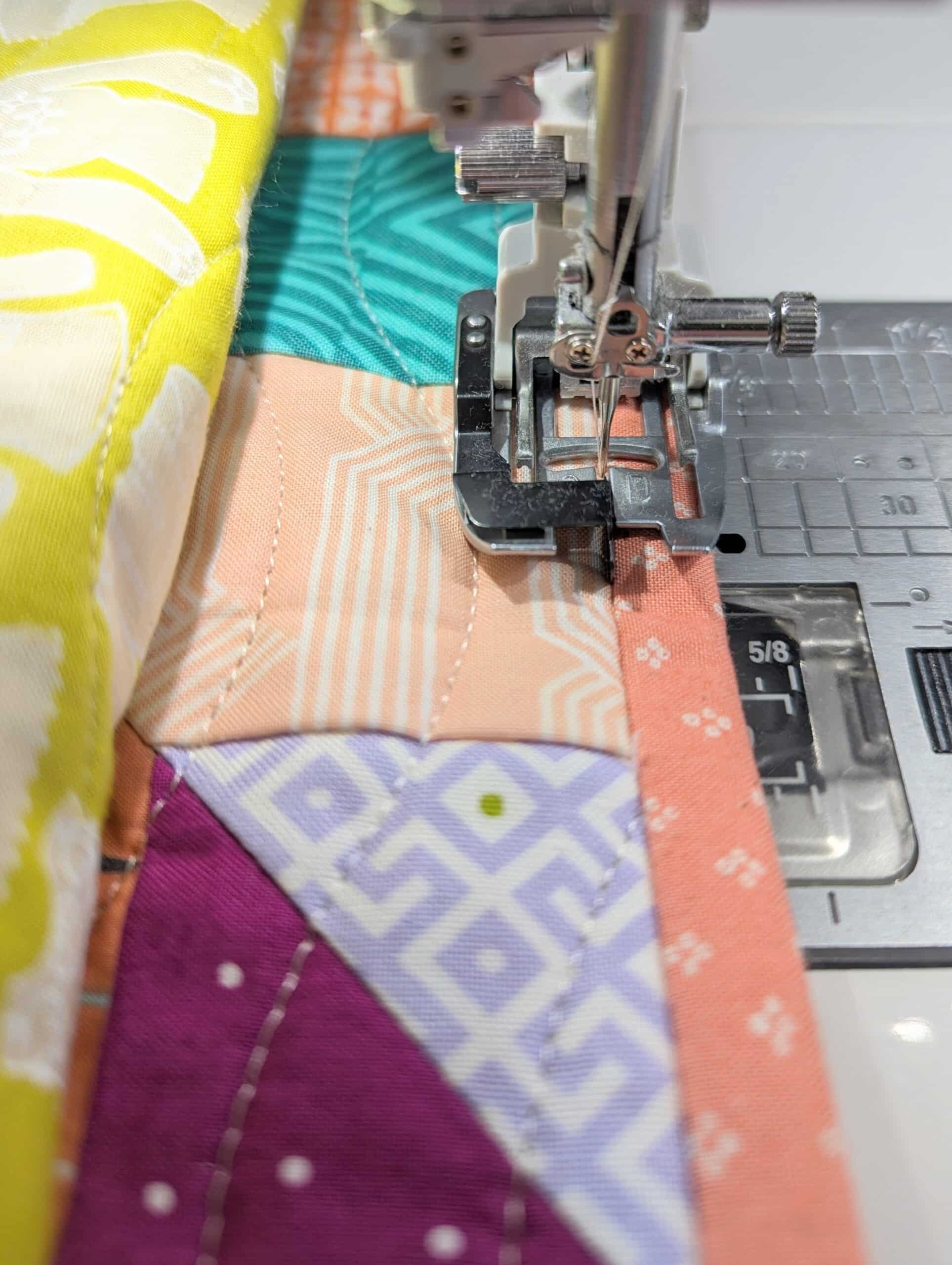 The needle of a sewing machine stitching the binding to a quilt.