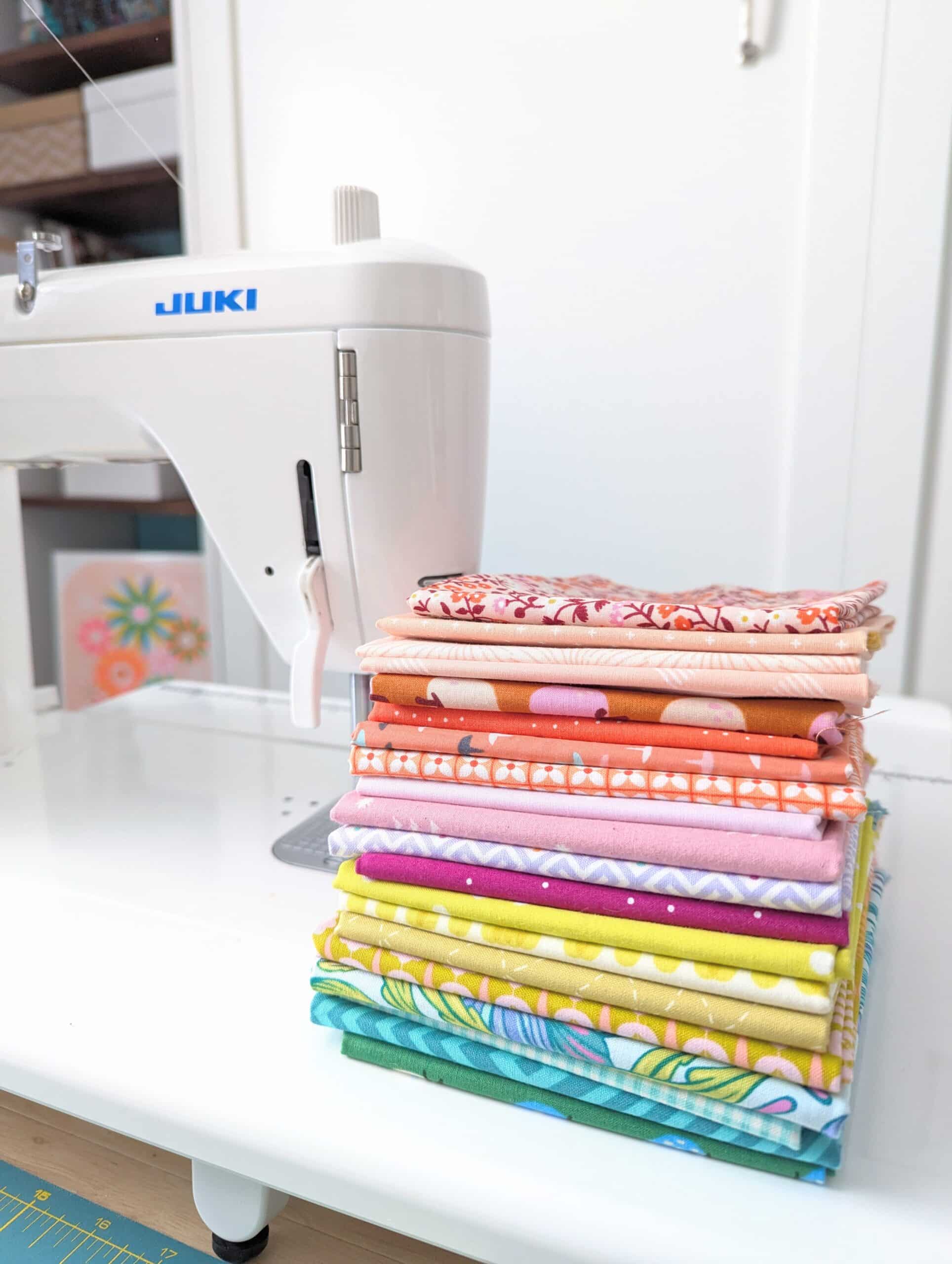 A stack of fat quarters sits on the bed of a sewing machine.