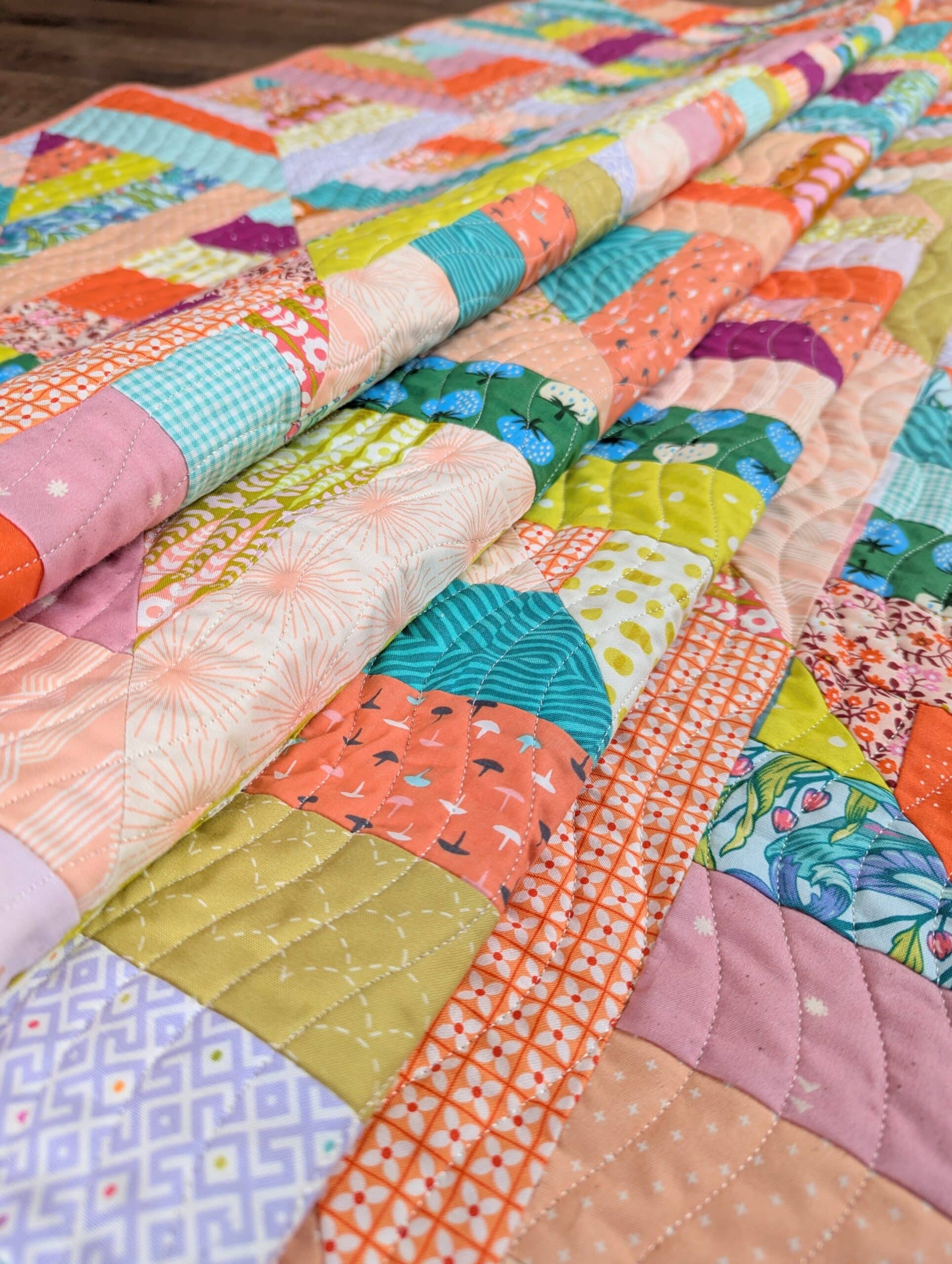 The finished quilt lies on the ground, folded over several times.