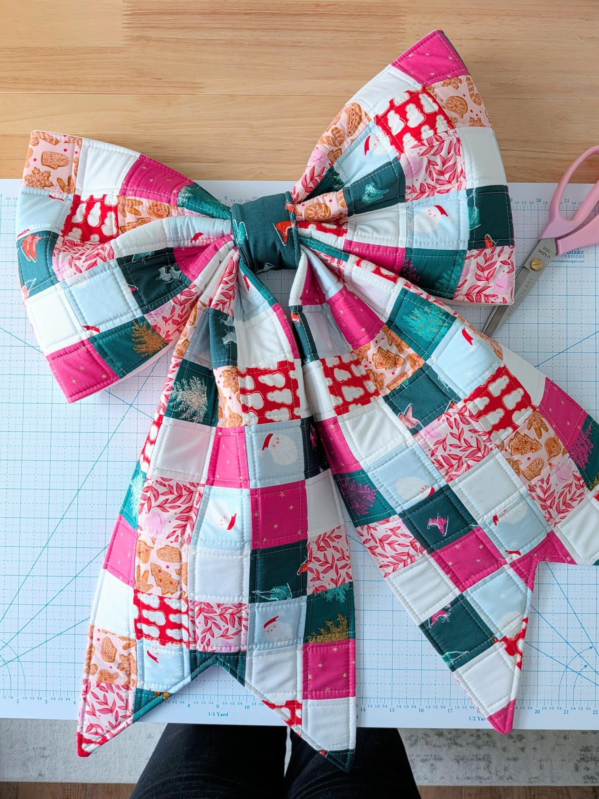 A patchwork bow lies on a cutting mat with some scissors.