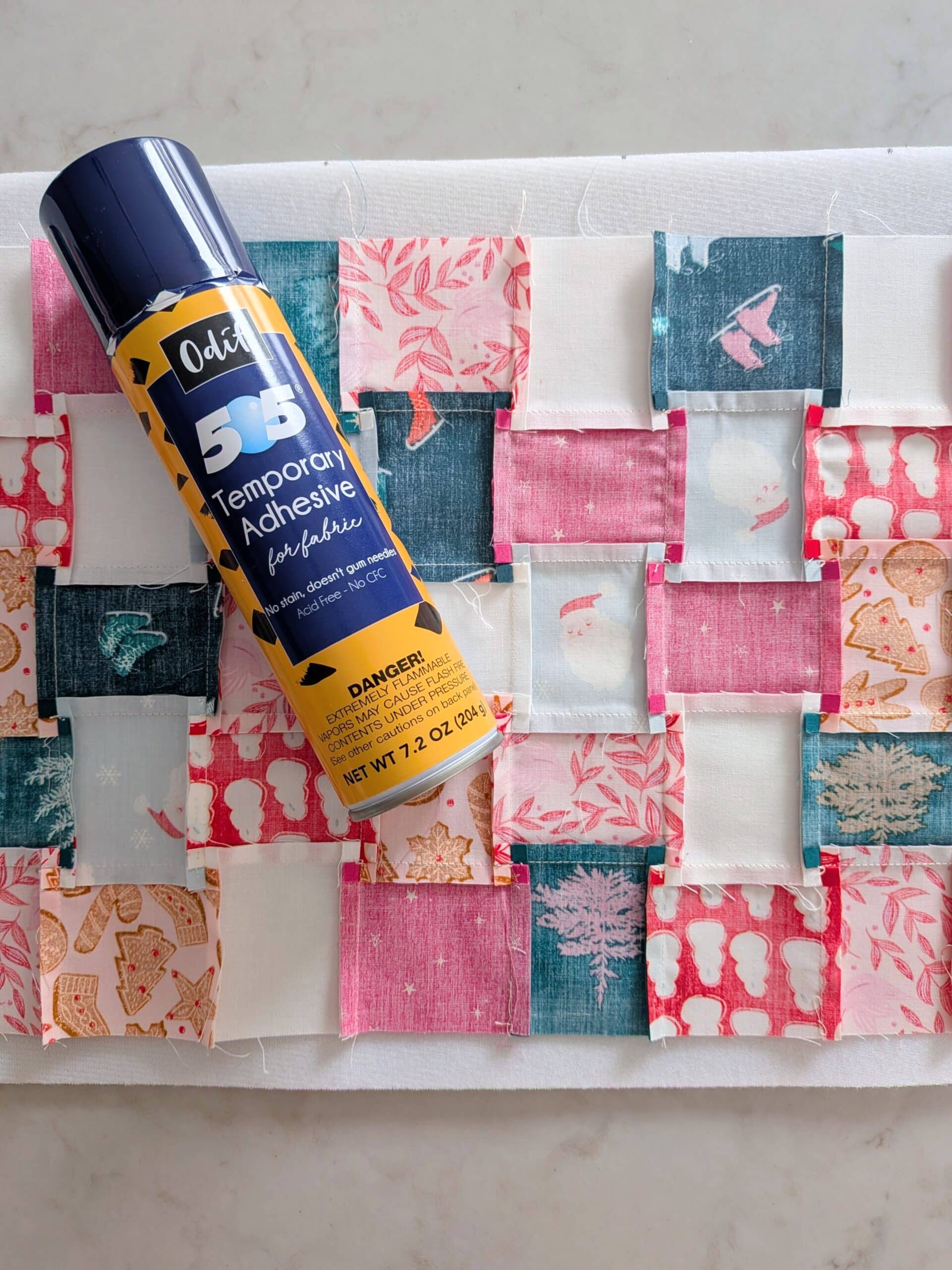 A patchwork panel lies face down on a piece of foam. A can of spray adhesive lies on top.