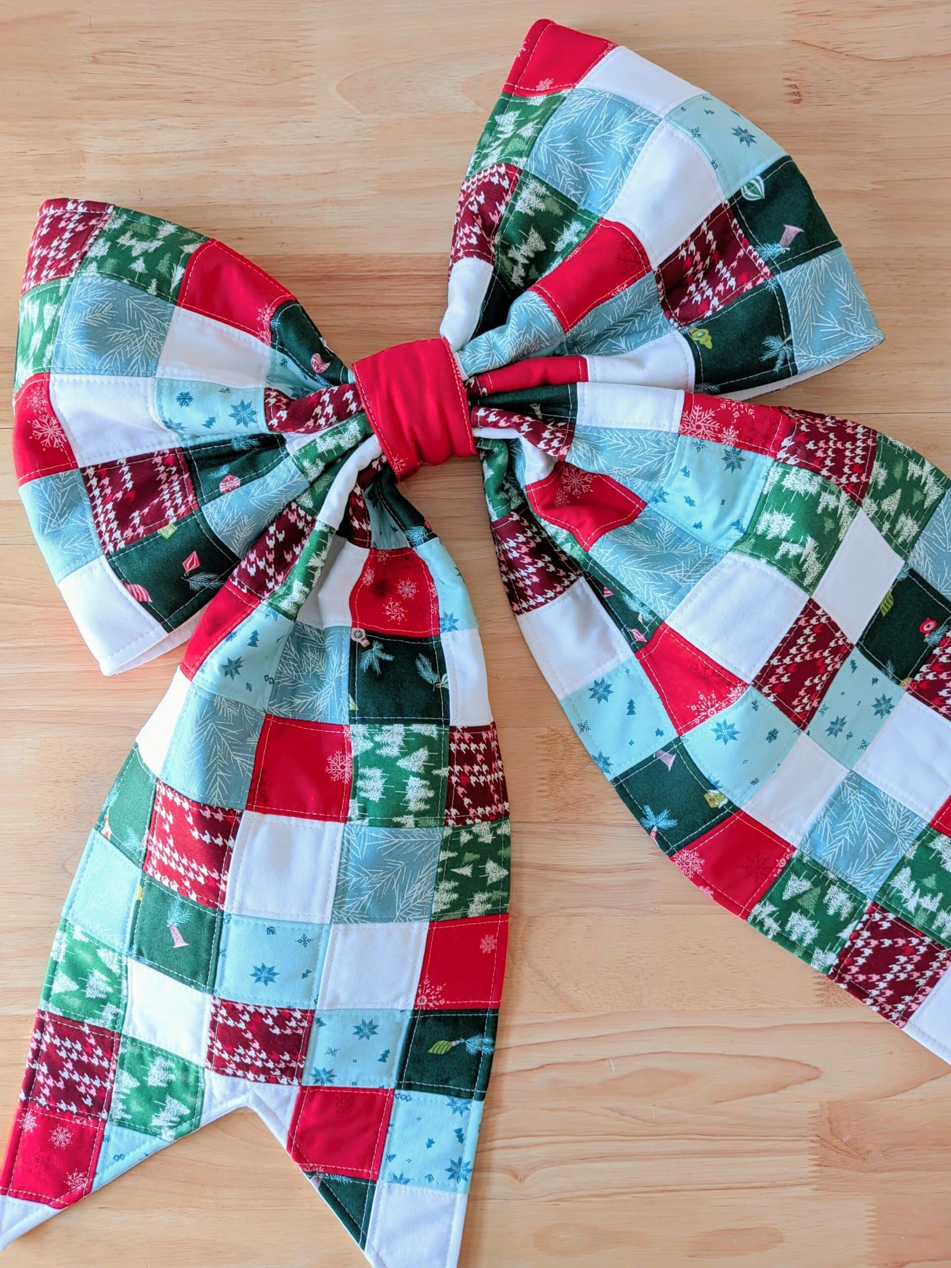 A quilted bow lays on a wooden work table.