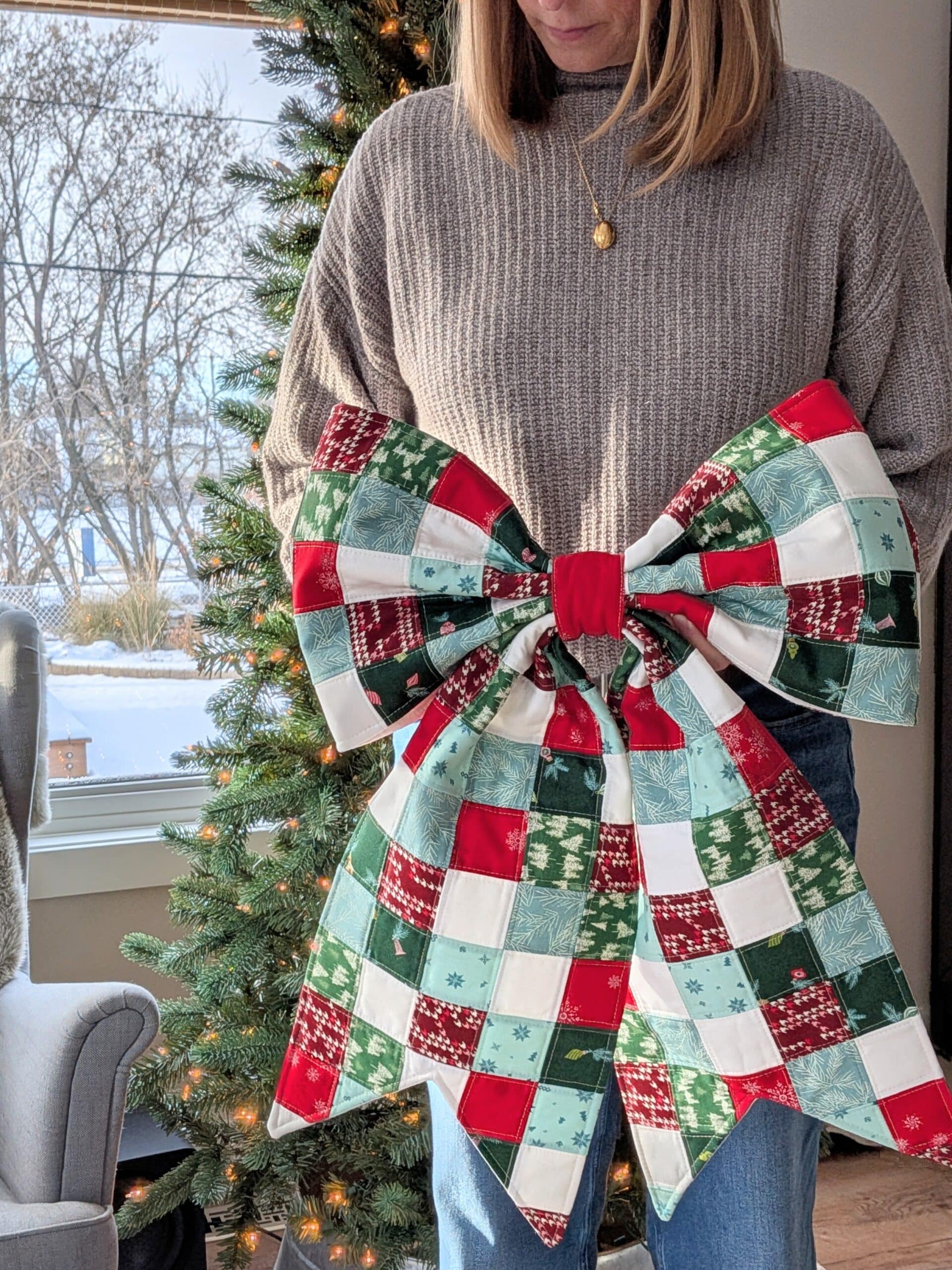 Shelly stands in front of a Christmas tree holding her quilted bow.