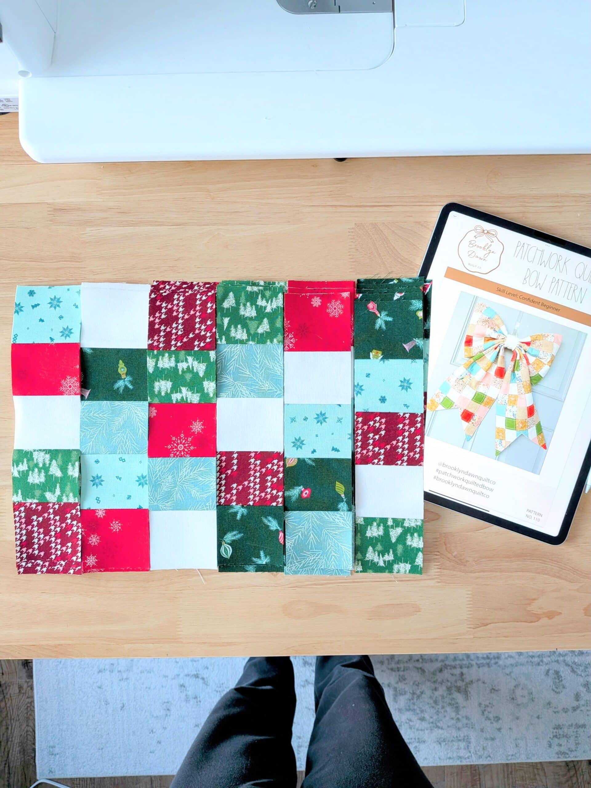 Strips of patchwork lie on a worktable with an iPad displaying the Patchwork Quilted Bow pattern.