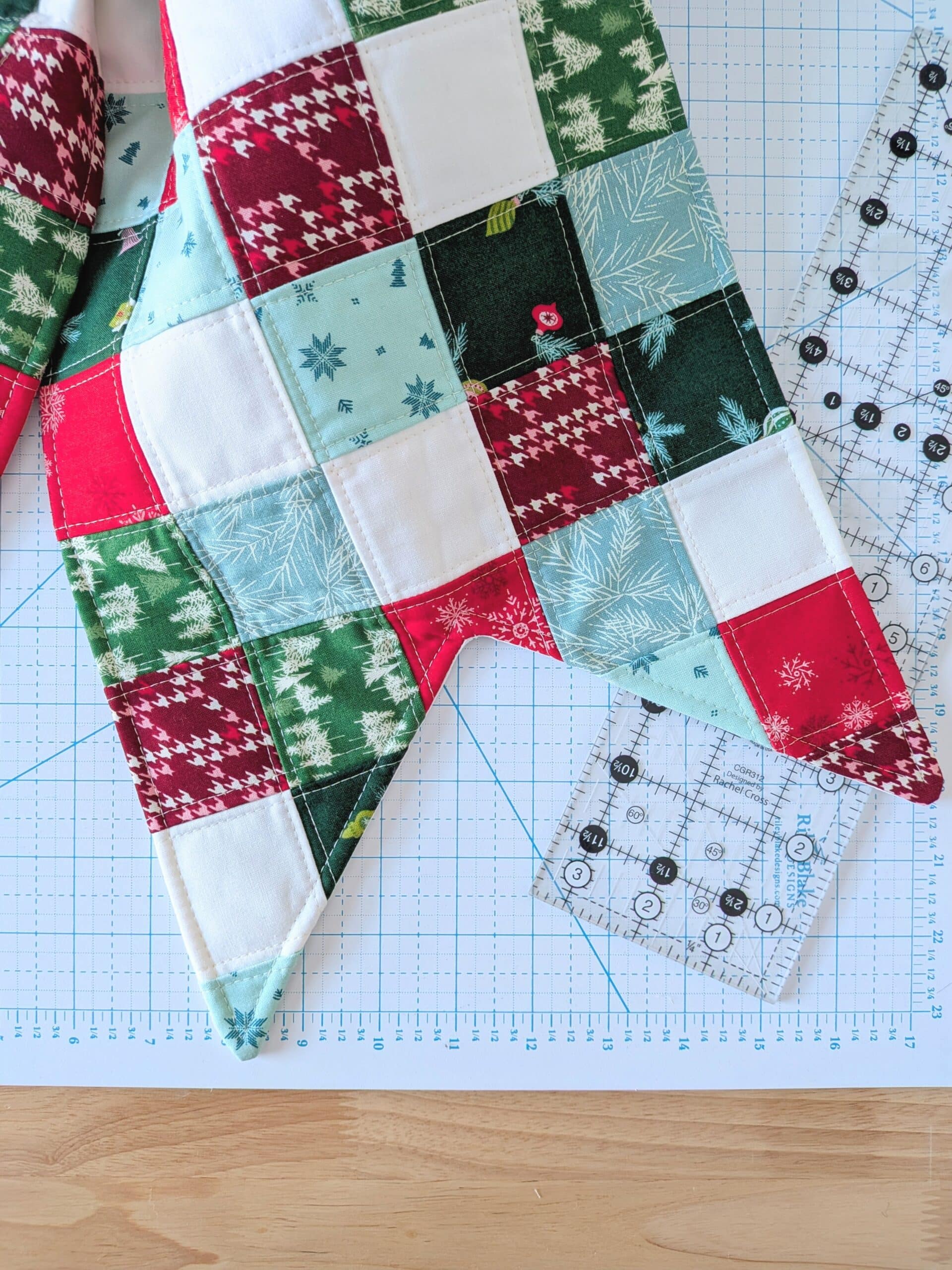The tail of a quilted bow lies on a worktable with a cutting mat and ruler.