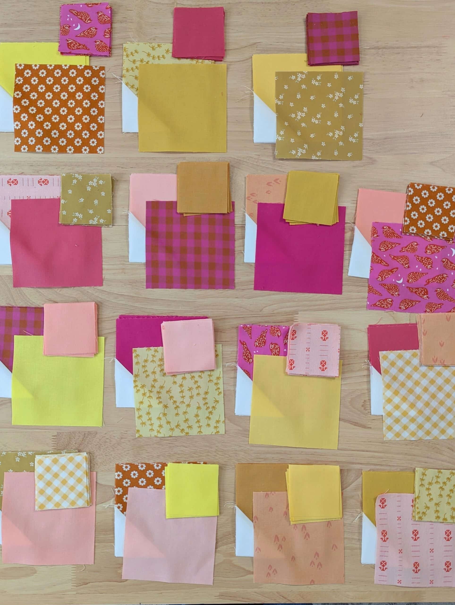 Colour pieces of fabric are arranged into 15 piles on a wooden desk.