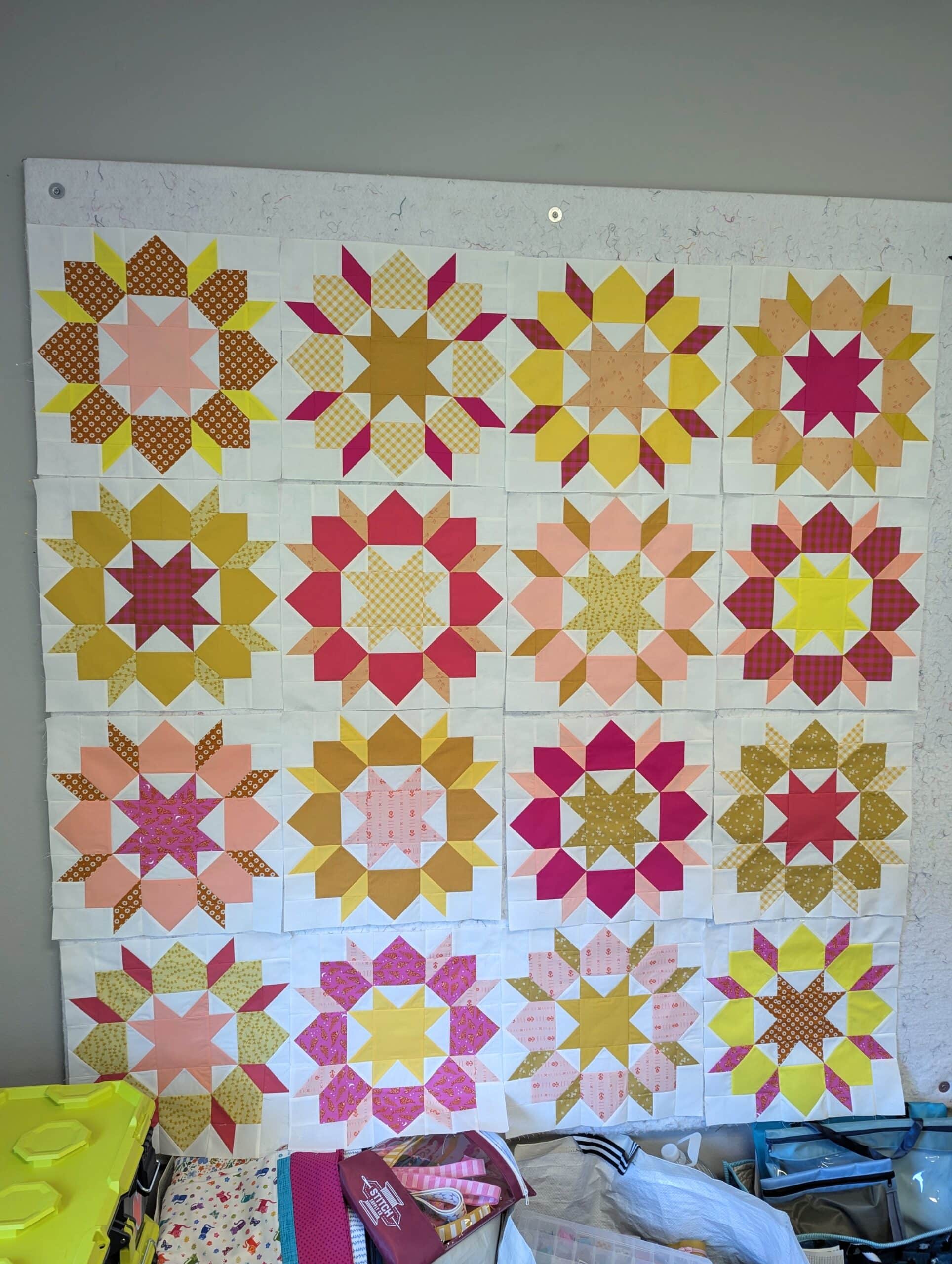 Sixteen quilt blocks are arranged on a white design wall.