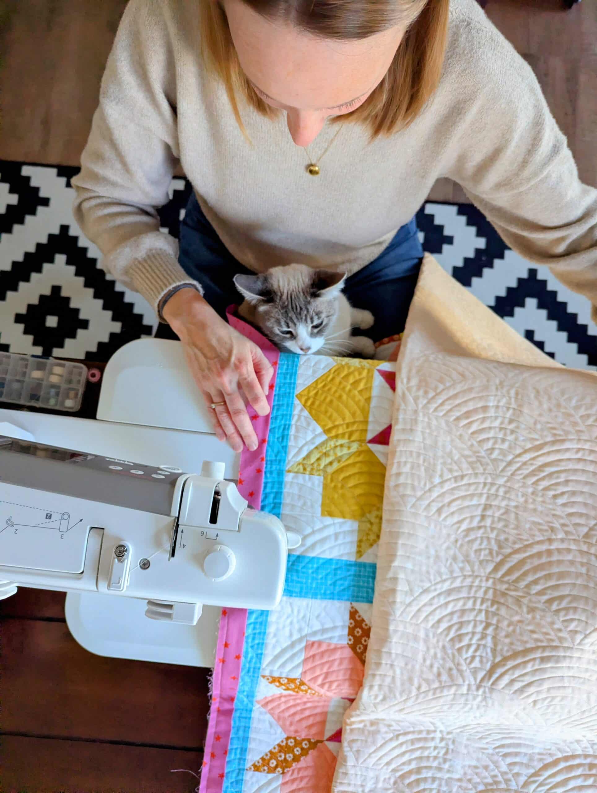 Shelly sits at the sewing machine with her cat Claire in her lap.