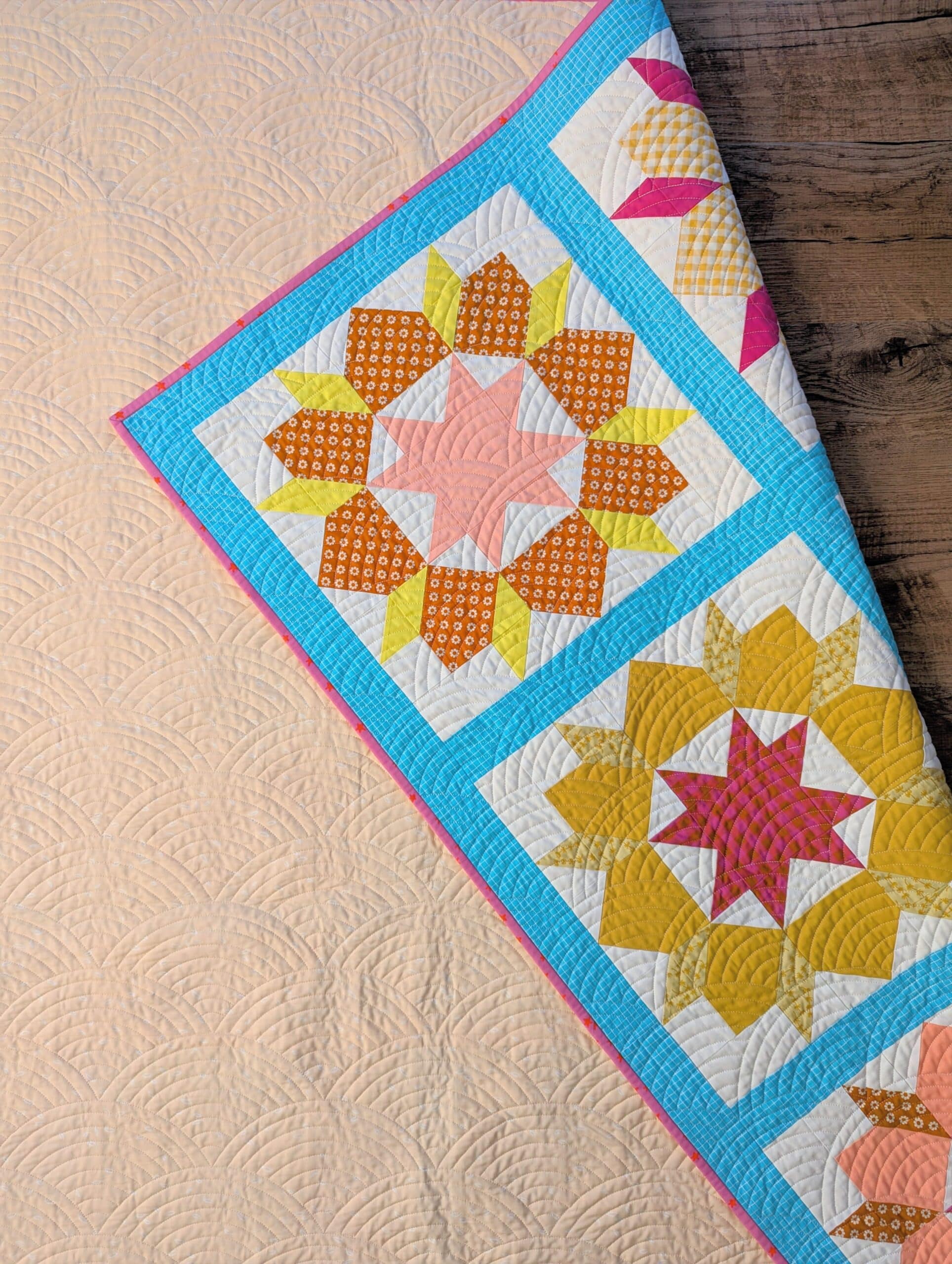 A bright and colourful quilt lies face down on a wooden floor, with one corner flipped over to reveal a peek of the front of the quilt.