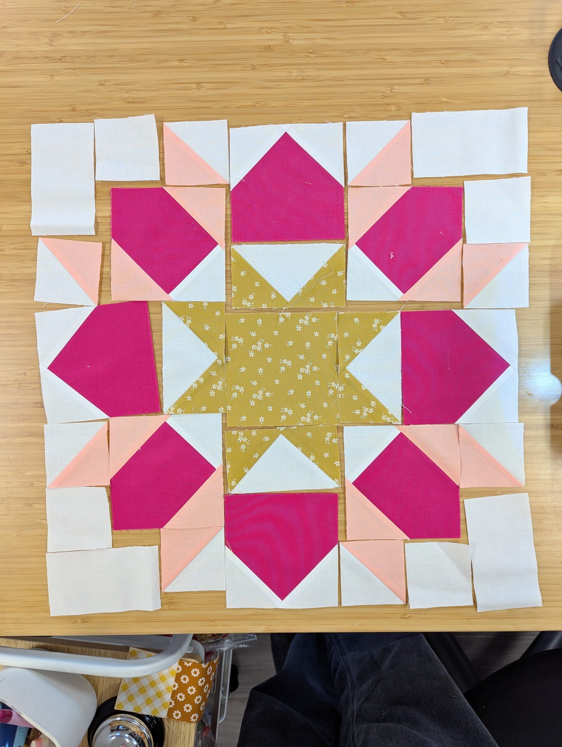 The sub units of a quilt block are arranged in order on a wooden desk.