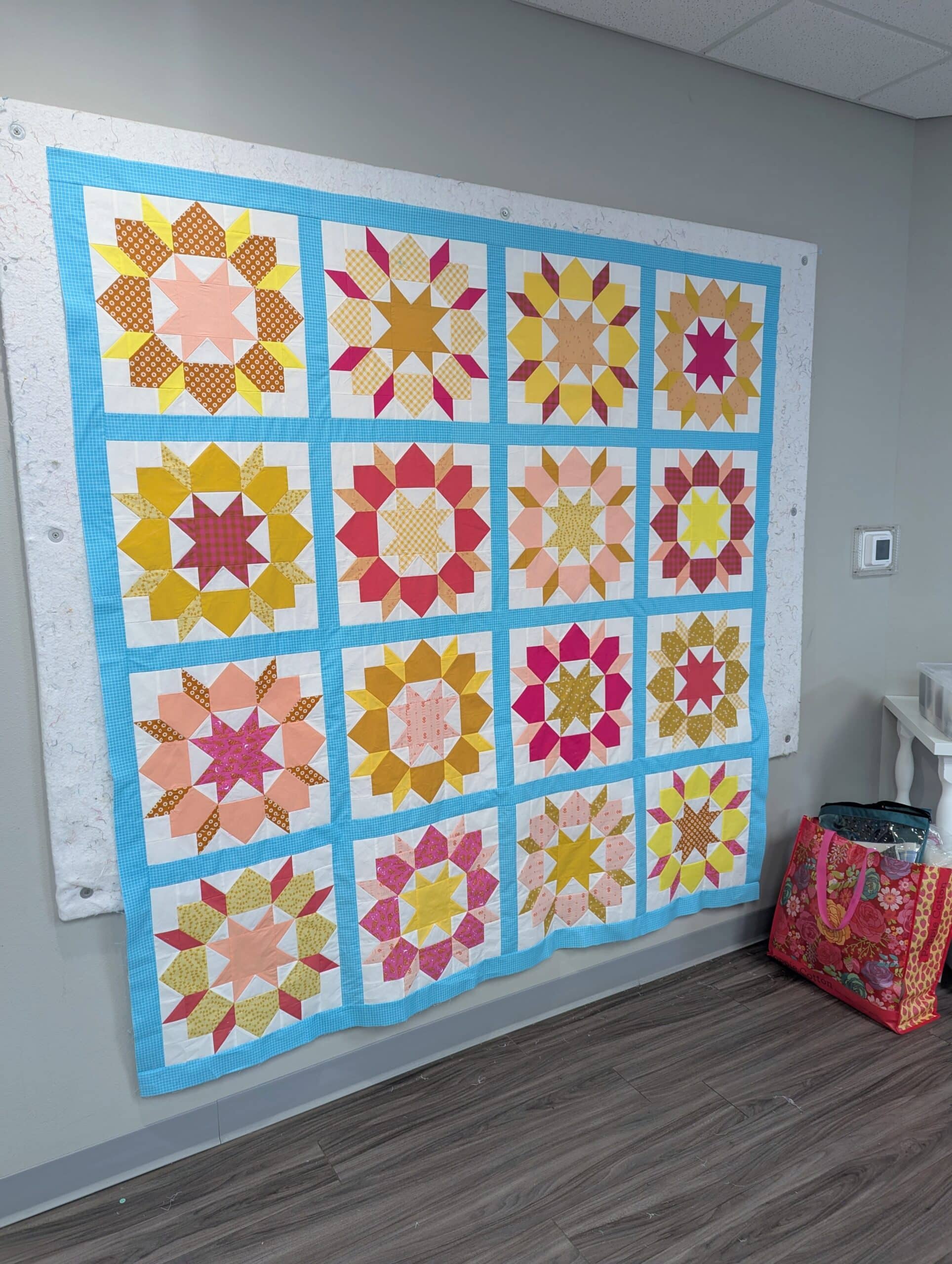 The completed quilt top hangs on a white design wall at a retreat center.
