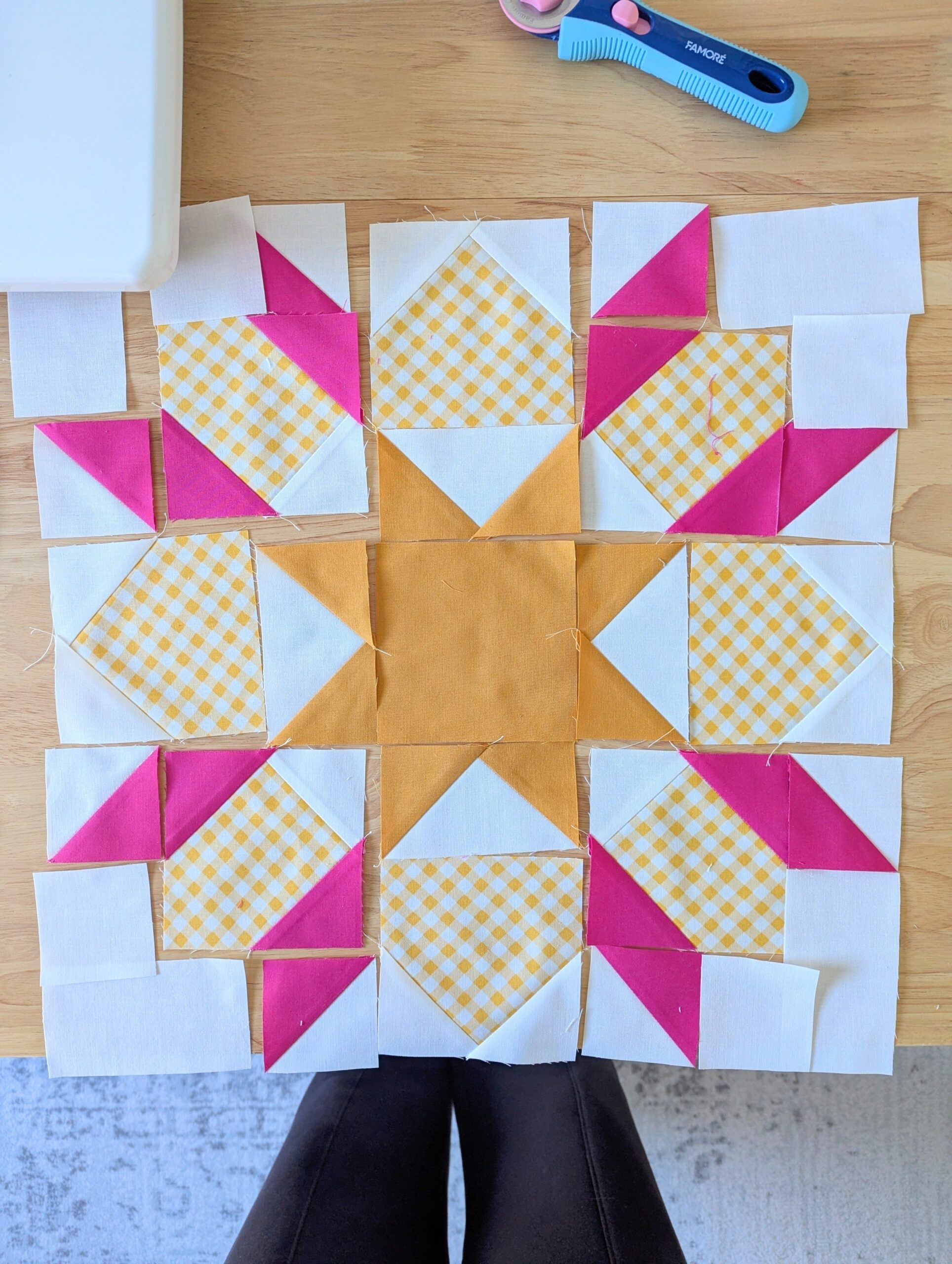 The pieces of a quilt block are arranged in order on a wooden desk.