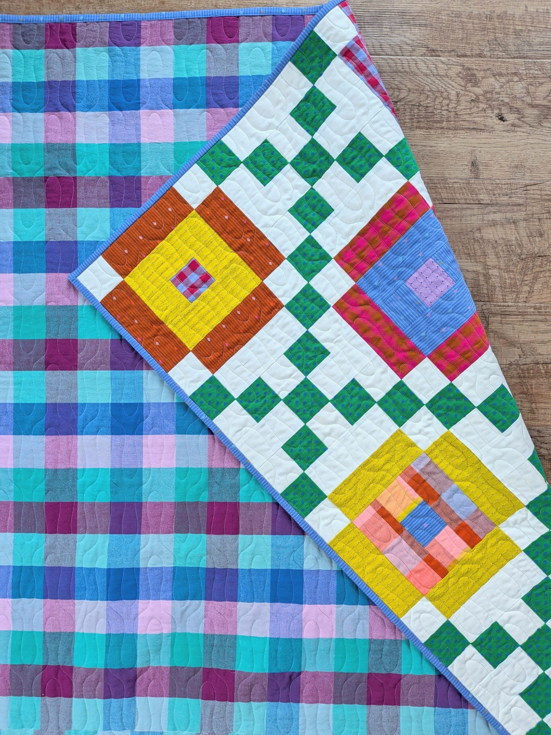 The finished quilt lies face down on a wooden floor, with one corner flipped over to reveal the front.