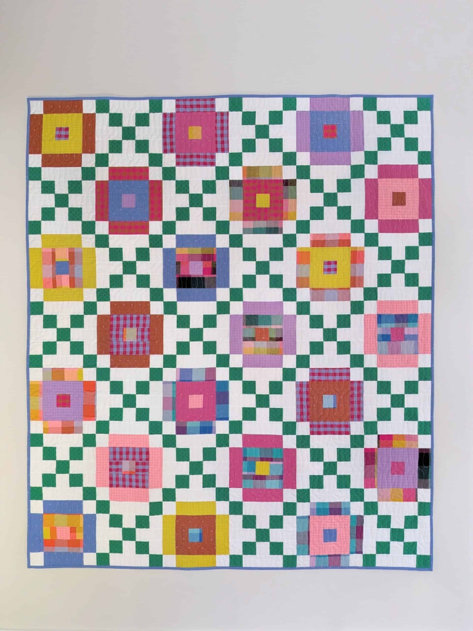 The finished quilt hangs on a blank wall.
