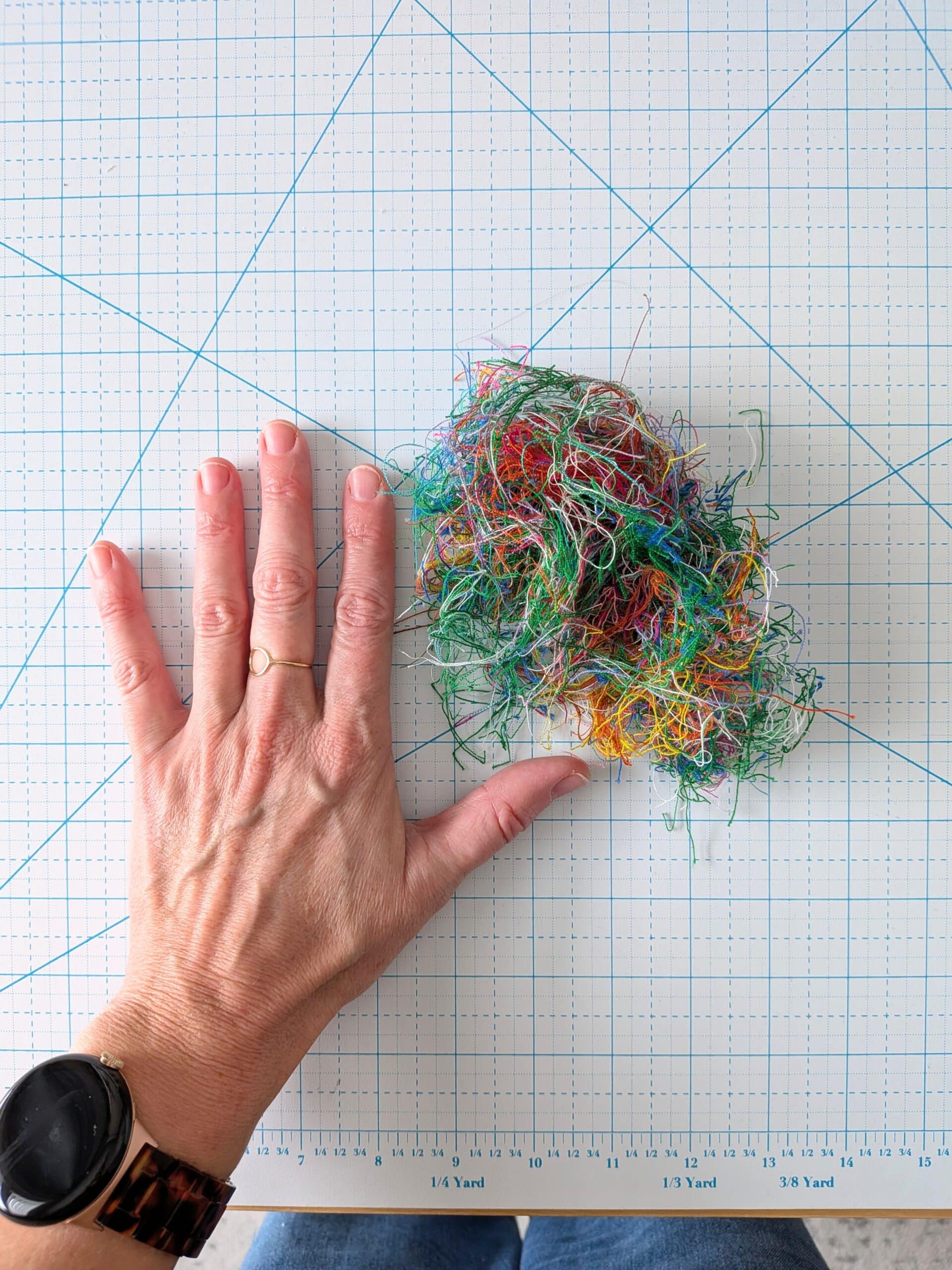 A large pile of thread trimmings sit on a cutting mat next to Shelly's hand for scale.