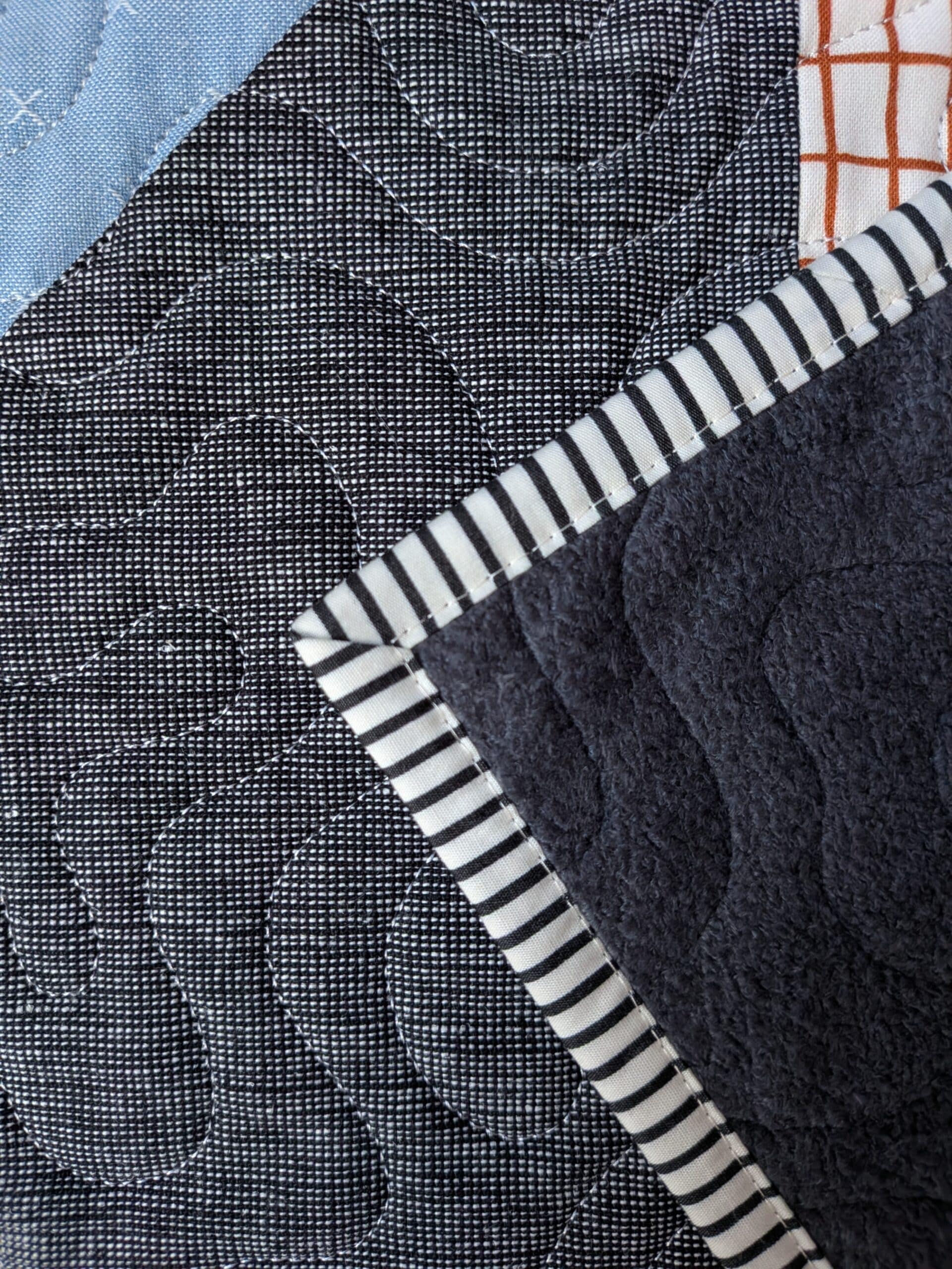 The corner of a quilt featuring striped binding is seen in a closeup view.