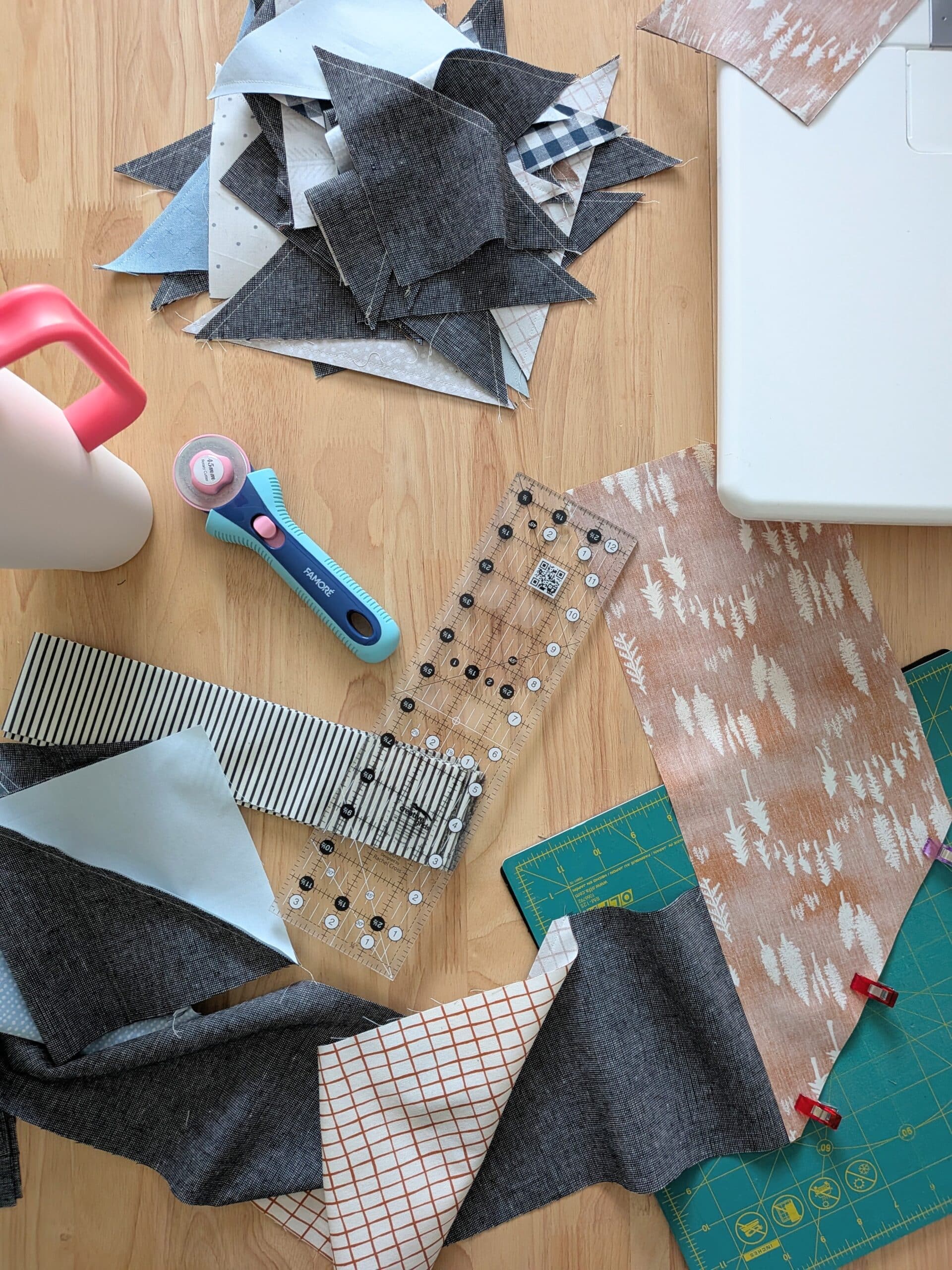 An overhead view of a sewing table with fabric, a ruler, a rotary cutter, and a water bottle in view.