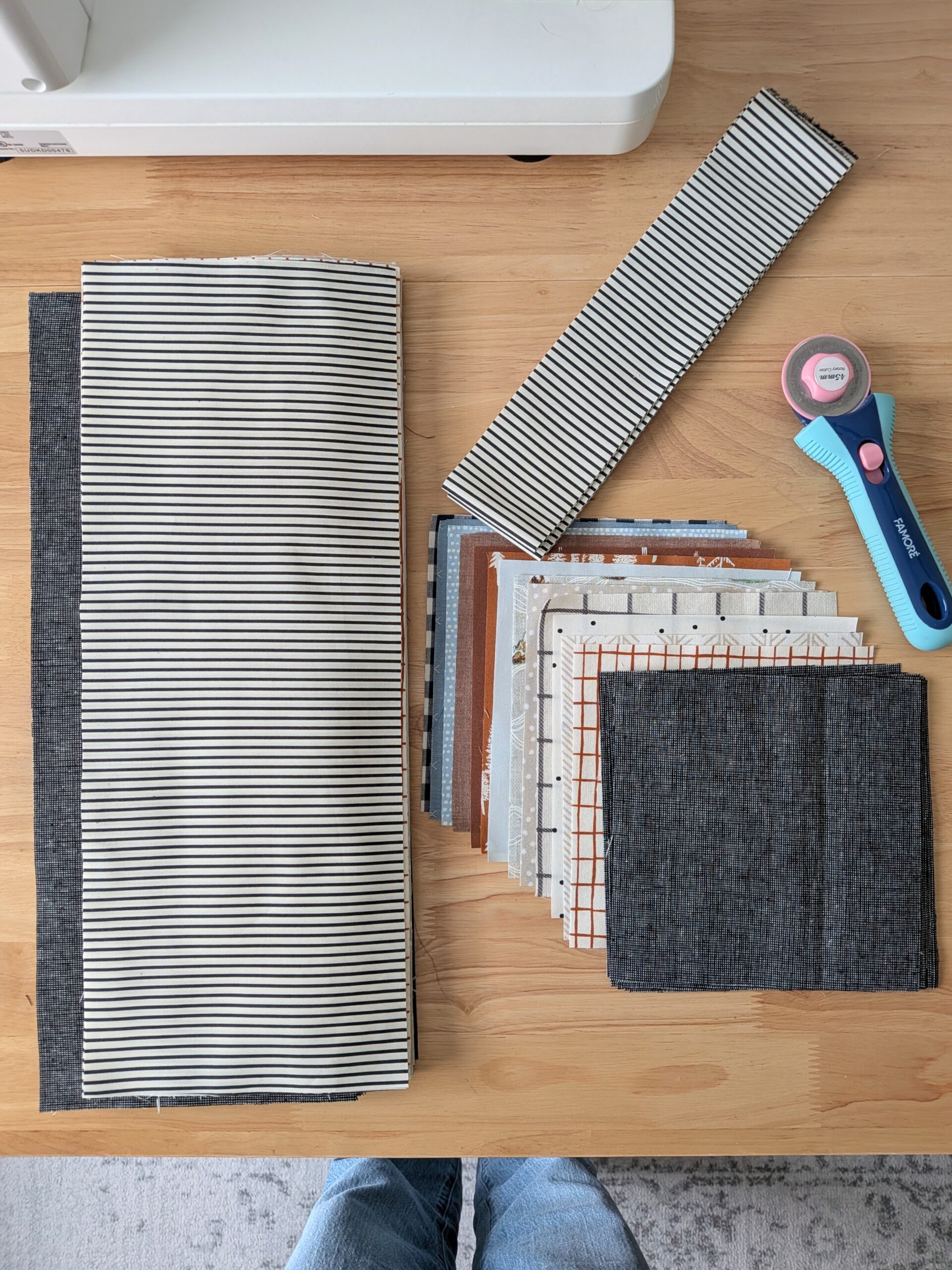 Large rectangles and smaller squares of fabrics are laid out on a wooden table.