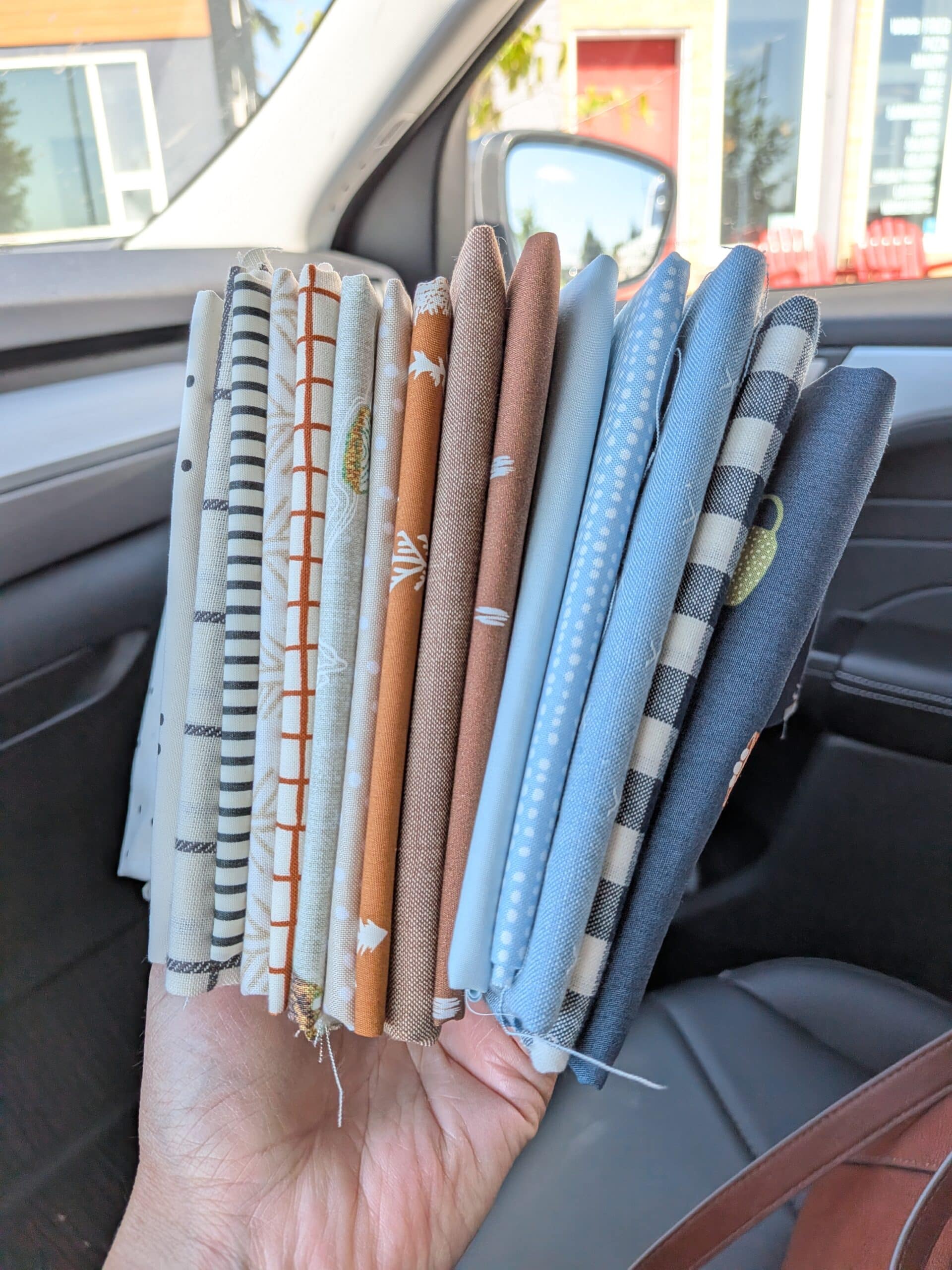 Shelly holds 15 small squares of fabric while sitting in her car.