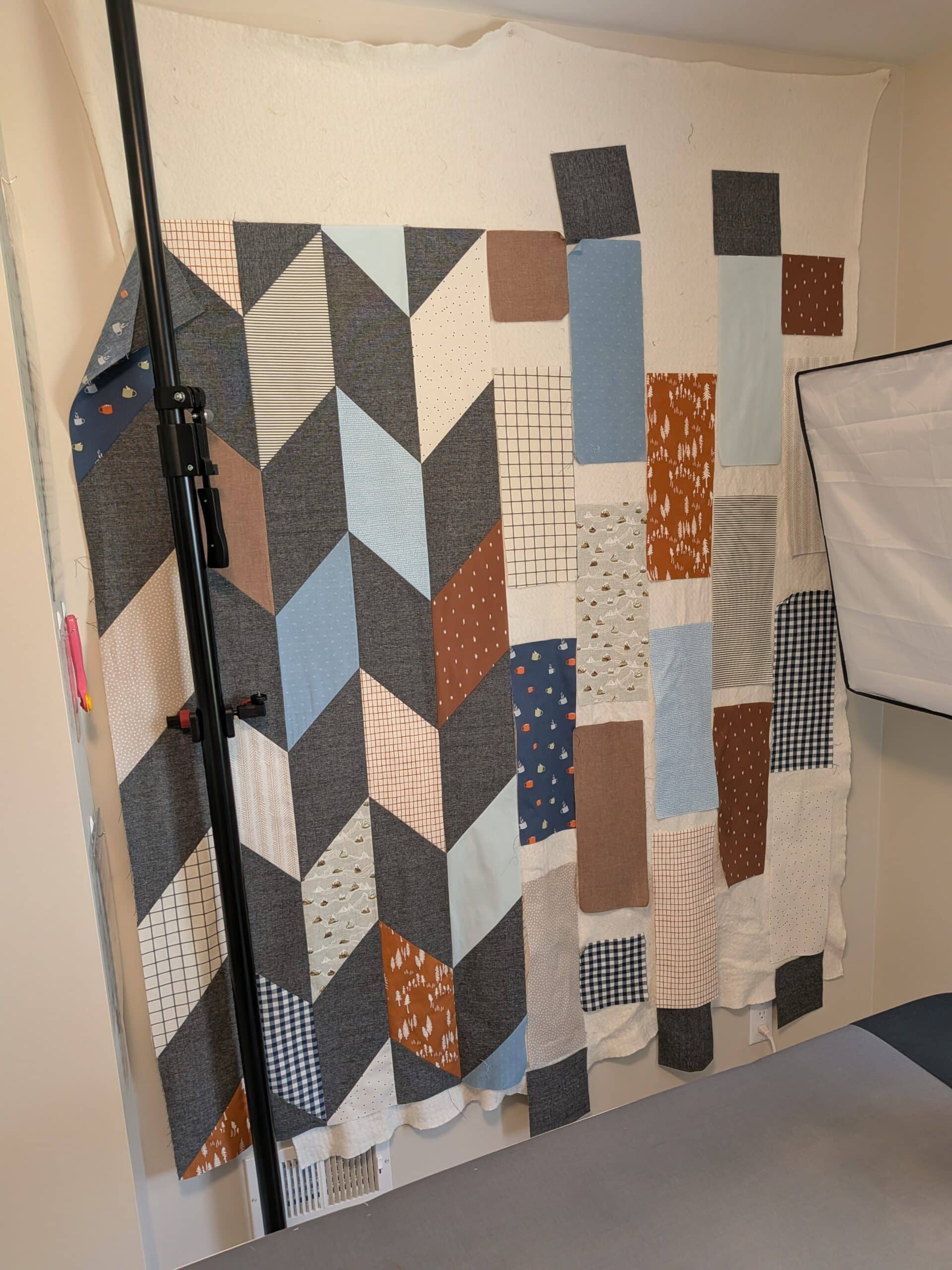 Five columns of a Chevron quilt are sewn together and hang side by side with several rectangles of fabric on a design wall.