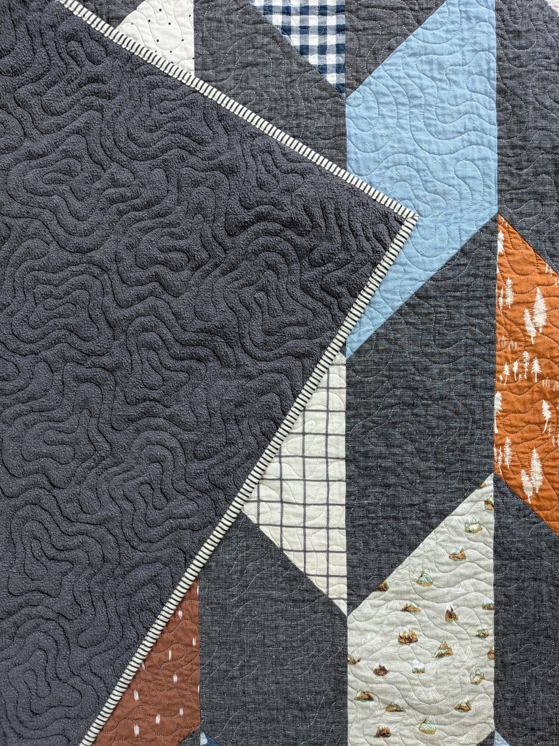 A chevron quilt lays face up, with one corner flipped over to reveal a fuzzy dark gray backing fabric.