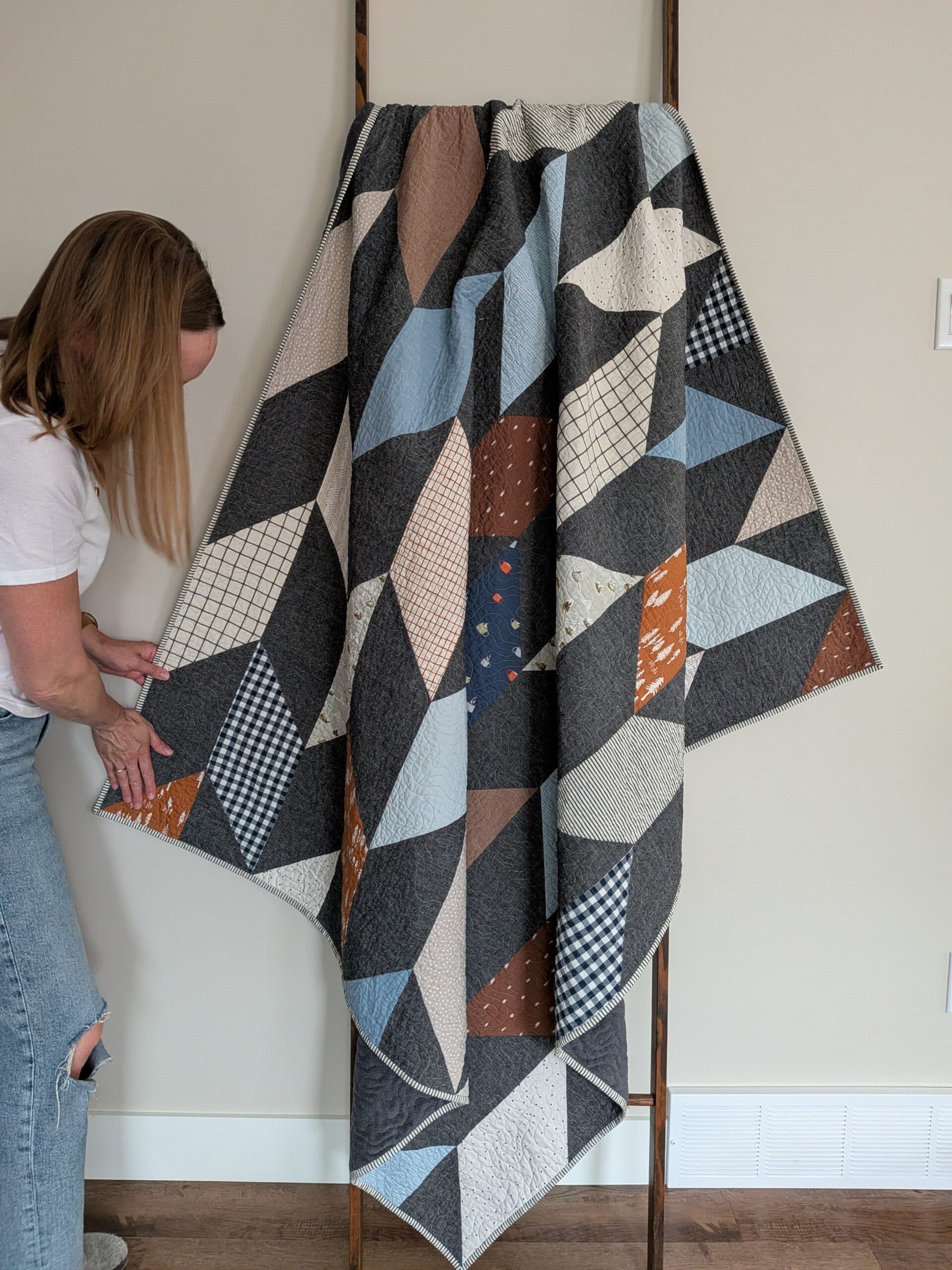 Shelly touches one corner of a chevron quilt as it hangs over a wooden ladder.