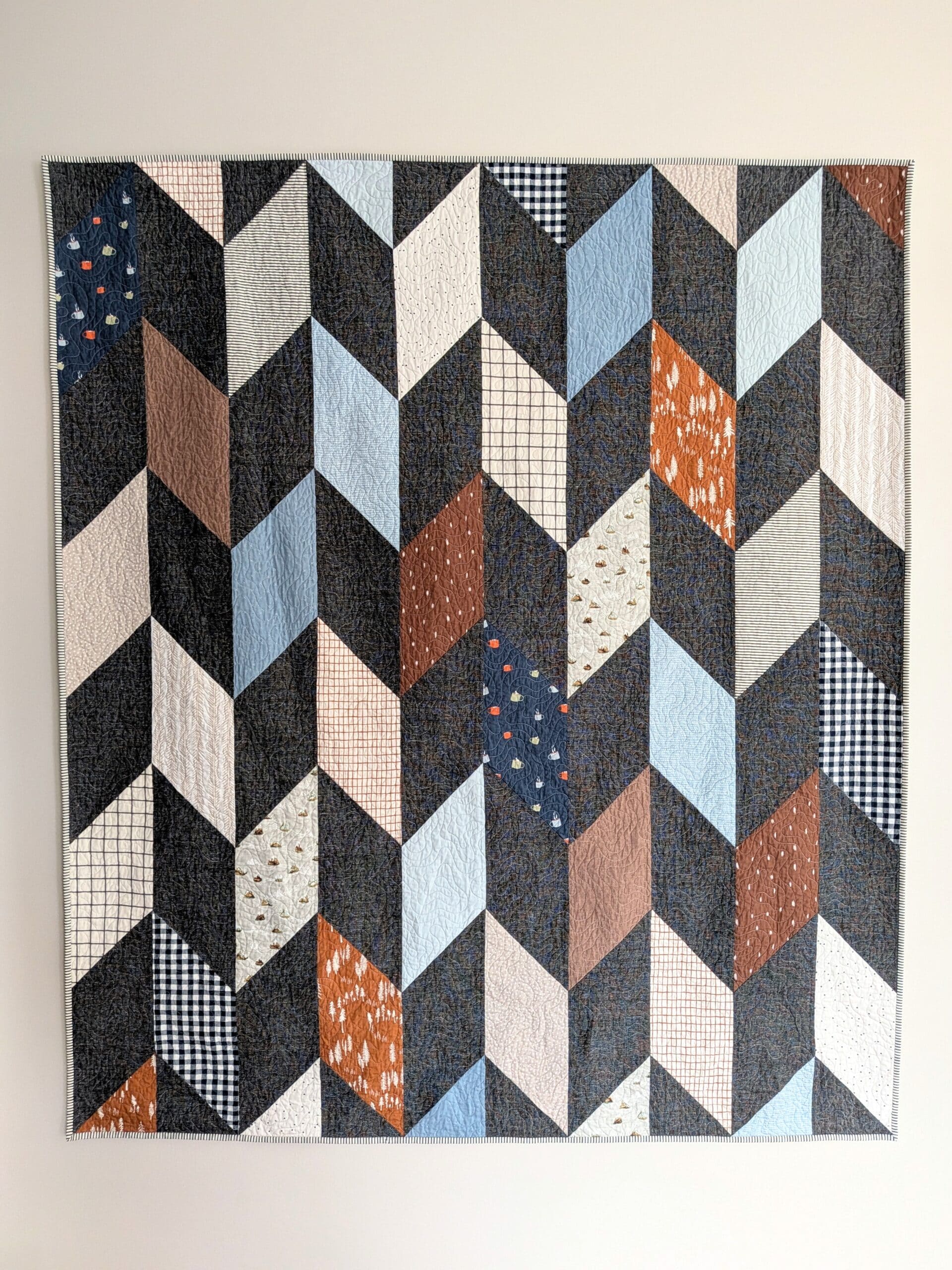 A chevron quilt is hung from a beige coloured wall.