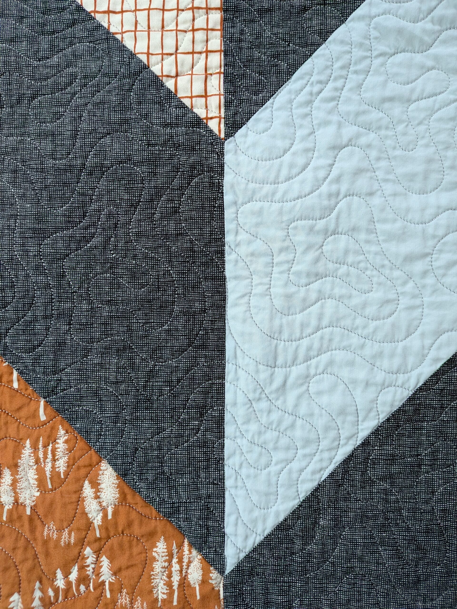 A dark gray and light blue quilt block are sewn together and quilted with a meandering design.