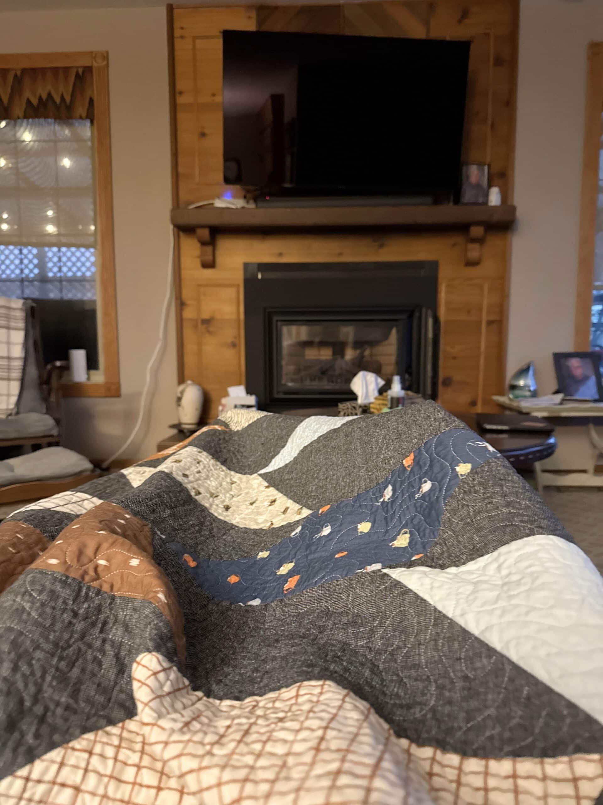 A chevron quilt is draped over Troy's legs as he sits in his living room.