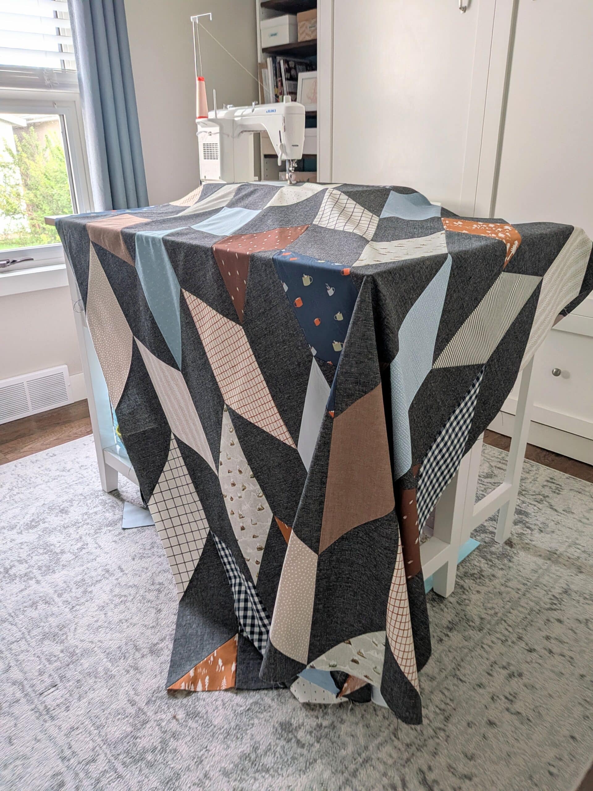 A chevron quilt top is draped over a sewing table.