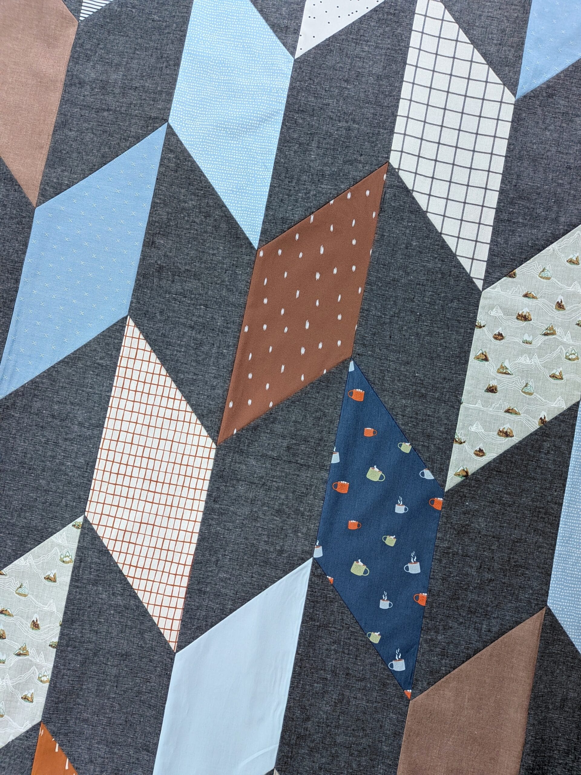 A completed chevron quilt top lays on the ground and is seen from overhead.