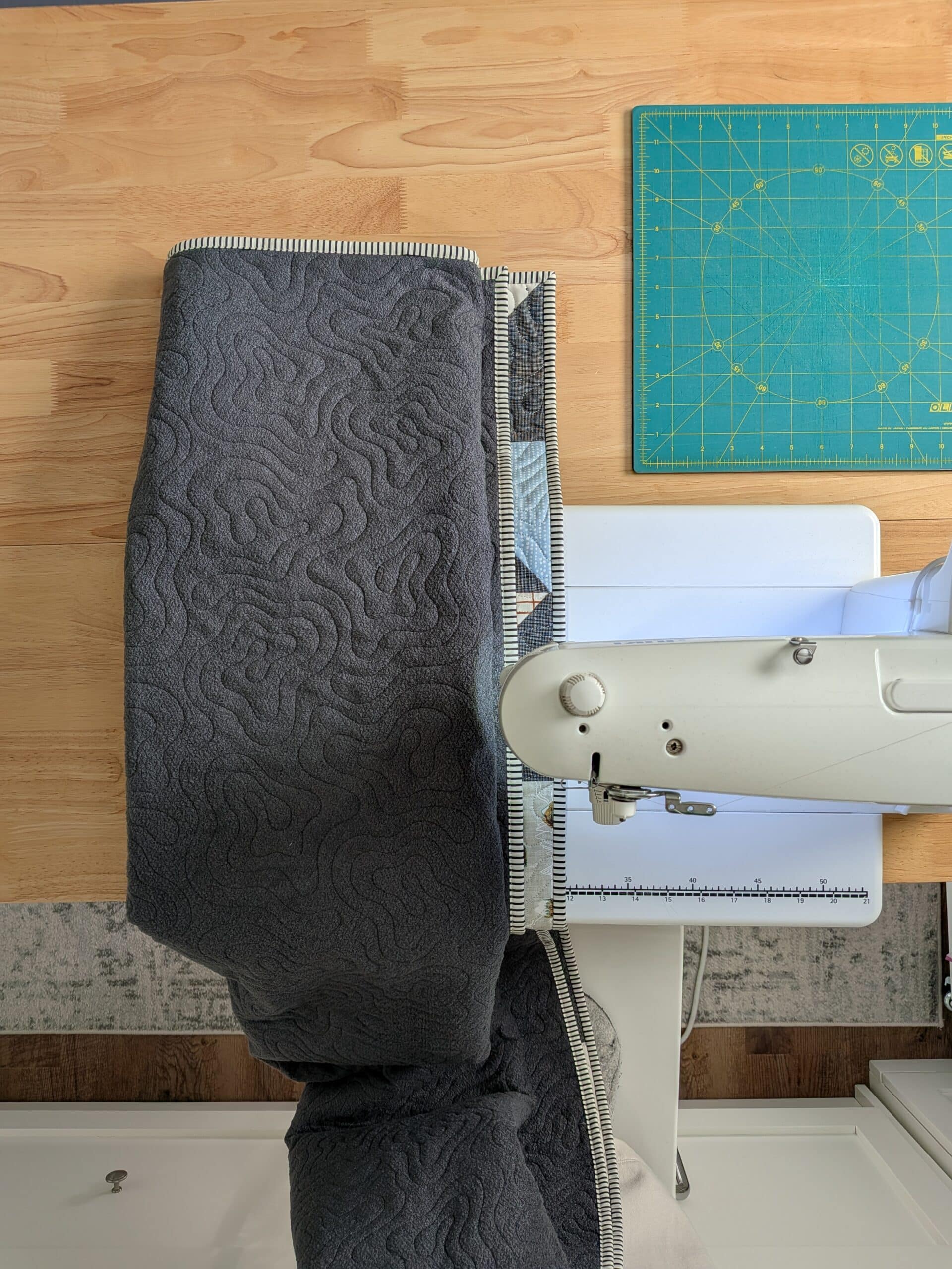 A quilt that has been folded into a long rectangle is seen from above as it passes through a sewing machine.
